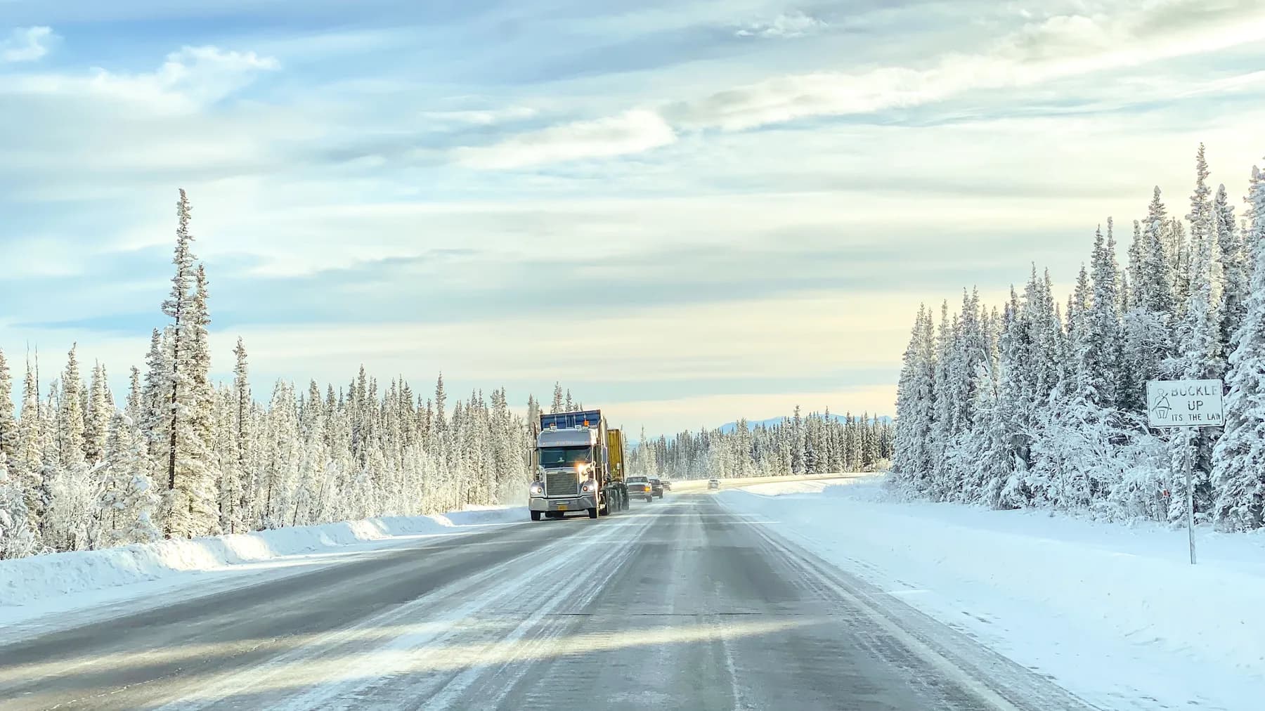 Lastbil på en snöig vinterväg kantad av snötäckta granar